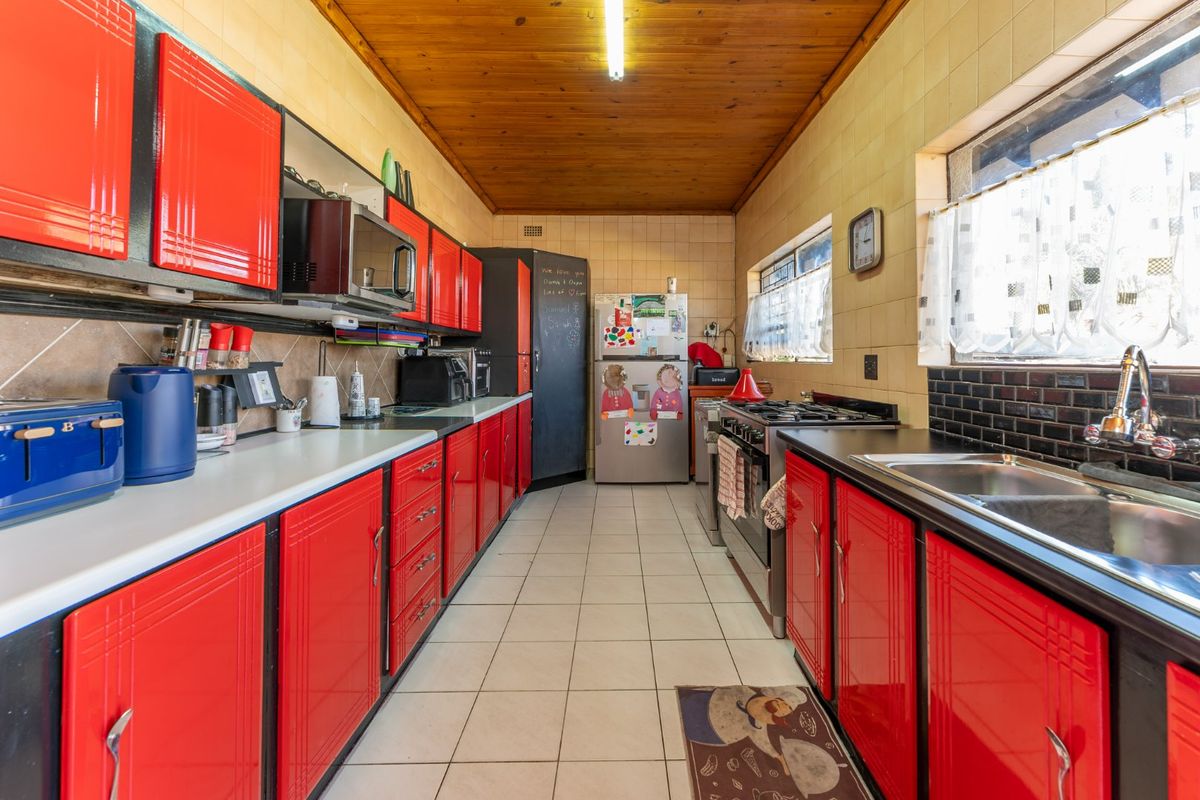A functional galley-style kitchen featuring vibrant red cabinetry, a gas stove, stainless steel sink, and a timber-paneled ceiling.