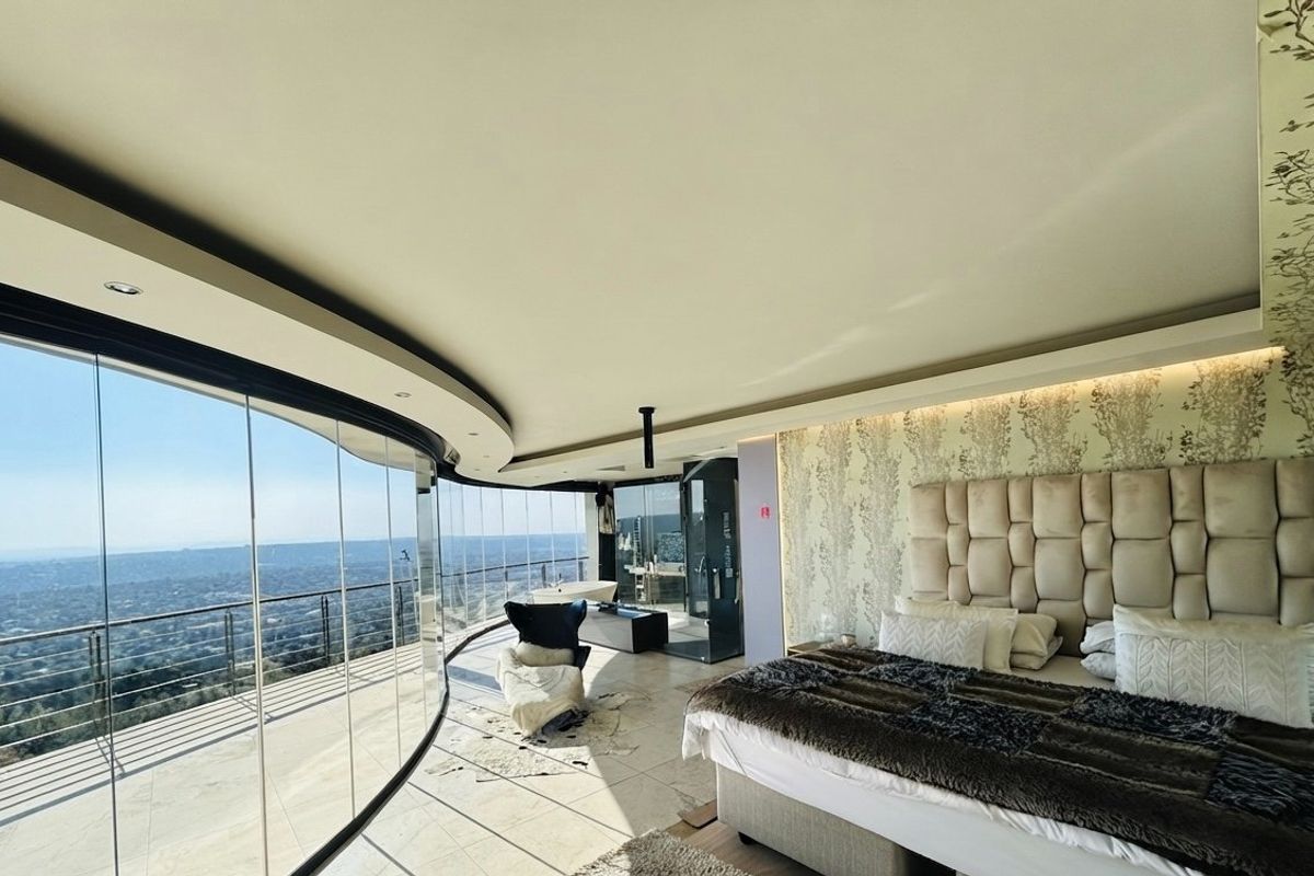 Luxurious master bedroom featuring expansive curved floor-to-ceiling glass walls with panoramic views, stone flooring, and an integrated ensuite bathroom.