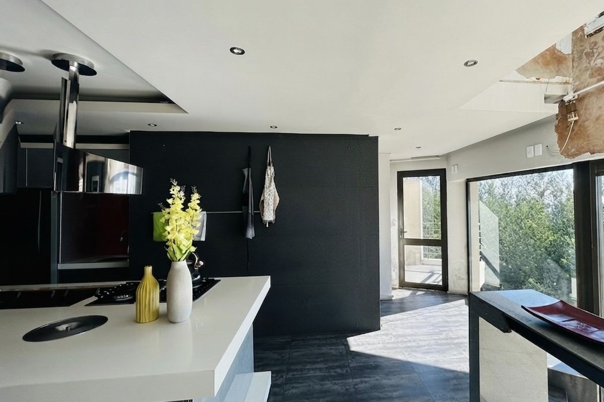 Modern kitchen featuring a central island with integrated hob and extractor, dark cabinetry, and large windows, currently requiring minor ceiling and wall repairs.