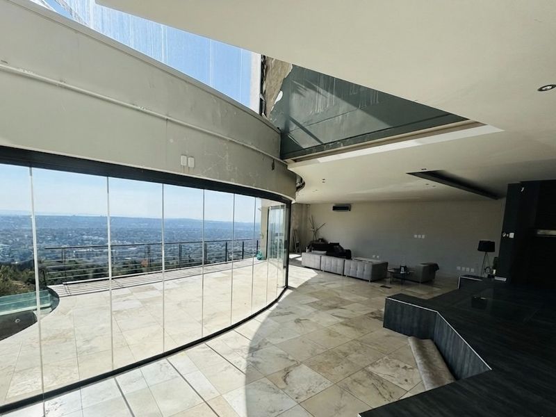 Expansive open-plan living area featuring curved floor-to-ceiling glass walls, stone tile flooring, and panoramic views, offering a bright and modern architectural space.