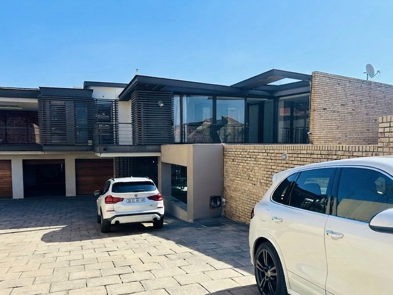 Modern multi-level residential facade featuring a paved driveway, double garage with timber doors, and contemporary architectural elements with large glass windows.