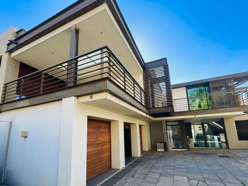 Modern double-storey residence featuring a paved driveway, integrated double garage with timber doors, and an expansive upper-level balcony with contemporary metal balustrades.