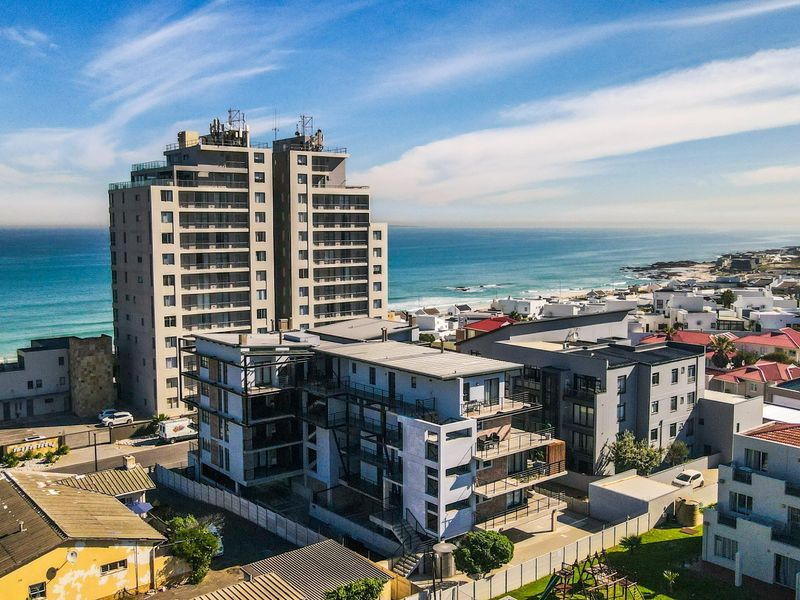 Aerial view of a modern townhouse complex situated in a coastal neighborhood, showcasing proximity to the ocean and surrounding residential infrastructure.