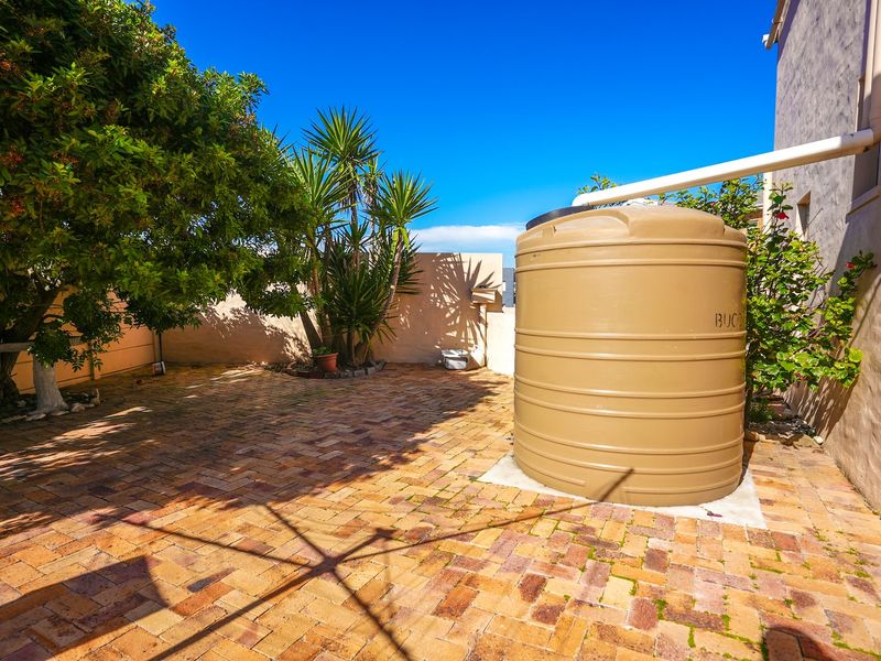 A rear courtyard area featuring brick paving, a boundary wall, and a large water storage tank connected to the building's downpipe system.