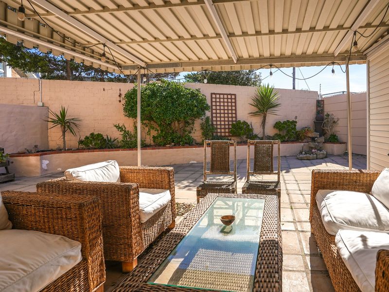 A covered outdoor patio area featuring paved flooring and a retaining wall with built-in garden beds, providing a functional space for outdoor relaxation.