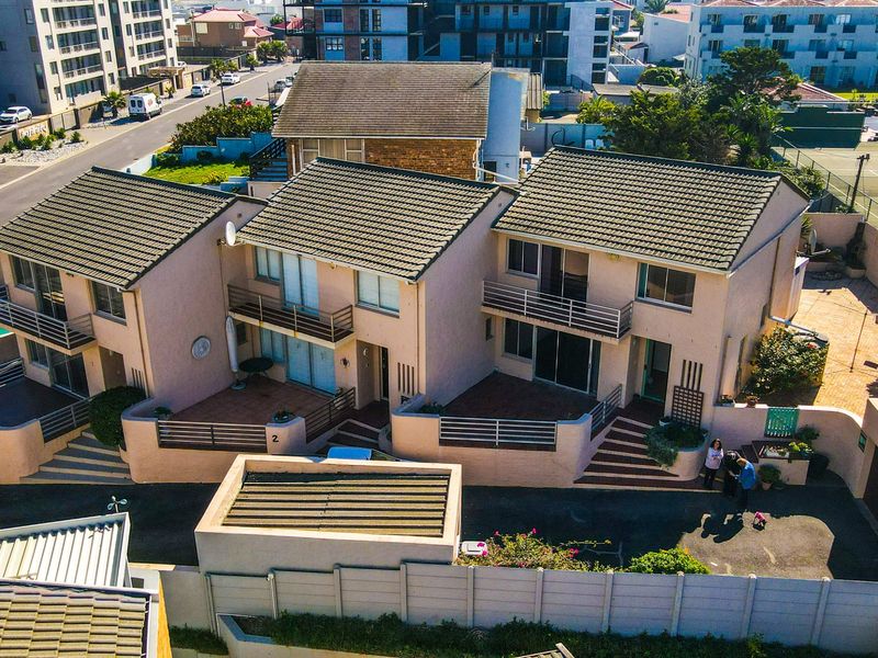 Aerial view of a townhouse complex featuring tiled roofs, private balconies, and paved patio areas within a residential estate setting.