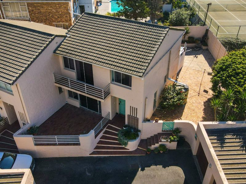 Aerial view of a townhouse featuring a tiled roof, balcony, paved courtyard, and established garden area within a residential complex.