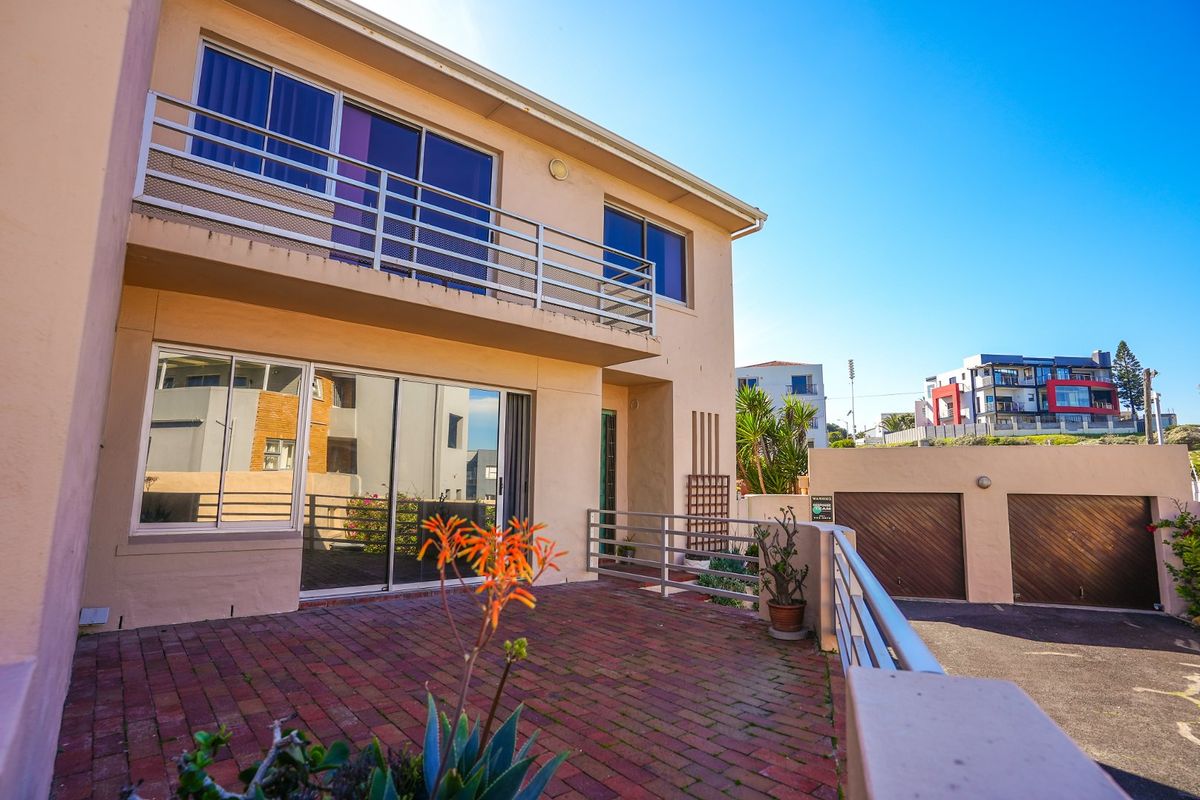 Rear view of the townhouse featuring a brick-paved patio, upper-level balcony with metal railings, and access to a double garage.