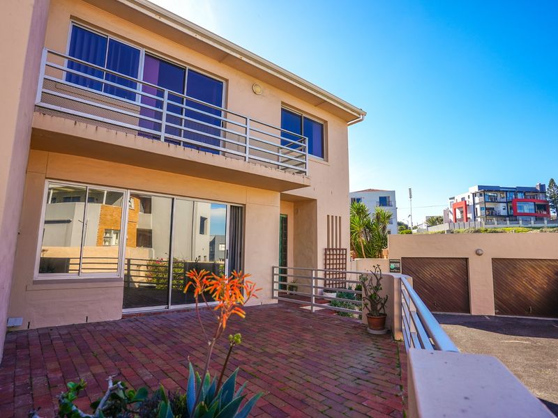 Rear view of the townhouse featuring a brick-paved patio, upper-level balcony with metal railings, and access to a double garage.