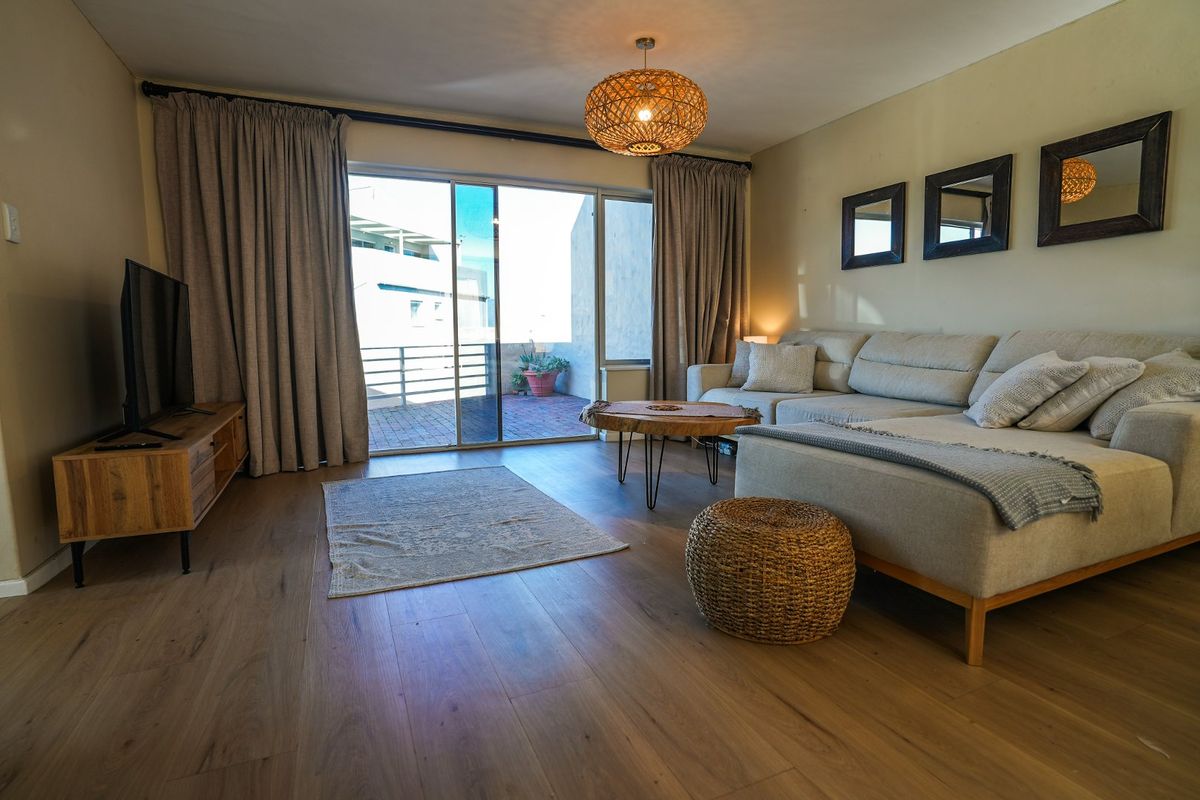 A well-maintained living room featuring laminate flooring and a large sliding glass door providing direct access to an outdoor patio area.