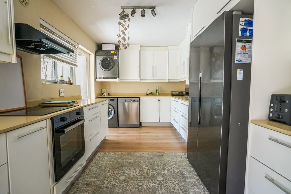 A functional kitchen featuring white cabinetry, built-in oven, electric hob, extractor fan, and integrated laundry appliances with wood-look laminate flooring.