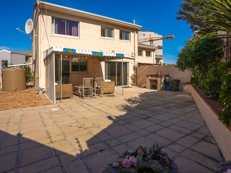 Rear exterior view of the townhouse featuring a paved patio area, built-in braai, and a water tank.