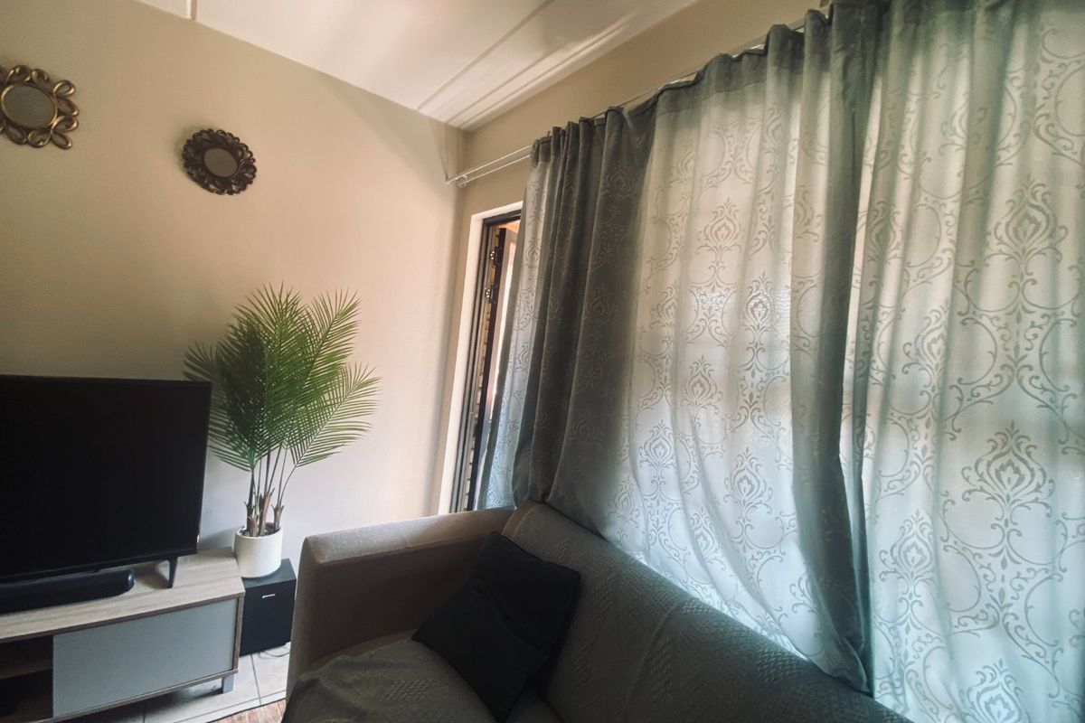 A cozy living room area featuring tiled flooring, decorative cornice detailing, and large window treatments allowing natural light into the space.