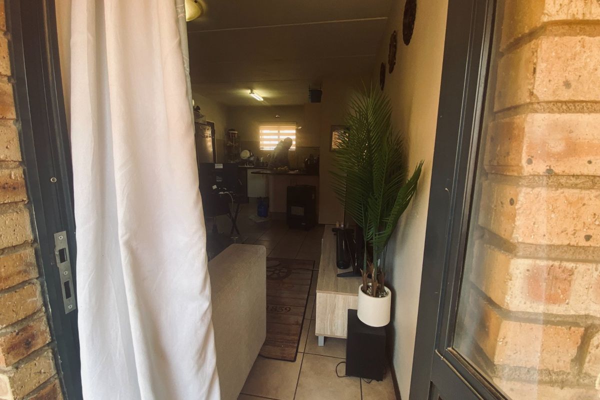 An open-plan living and kitchen area viewed from an exterior doorway, featuring tiled floors and exposed brick accents.