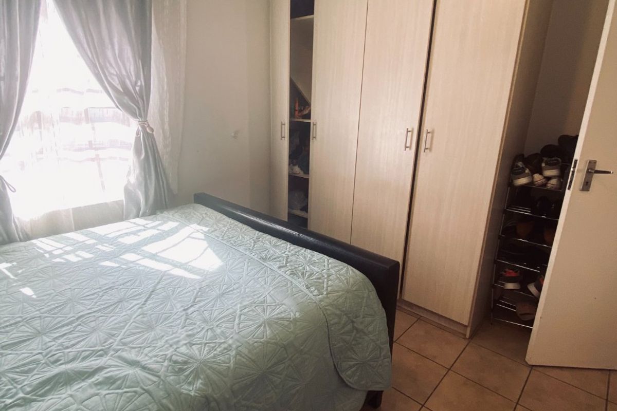 A functional bedroom featuring built-in cupboards, tiled flooring, and natural light through a window with curtains.