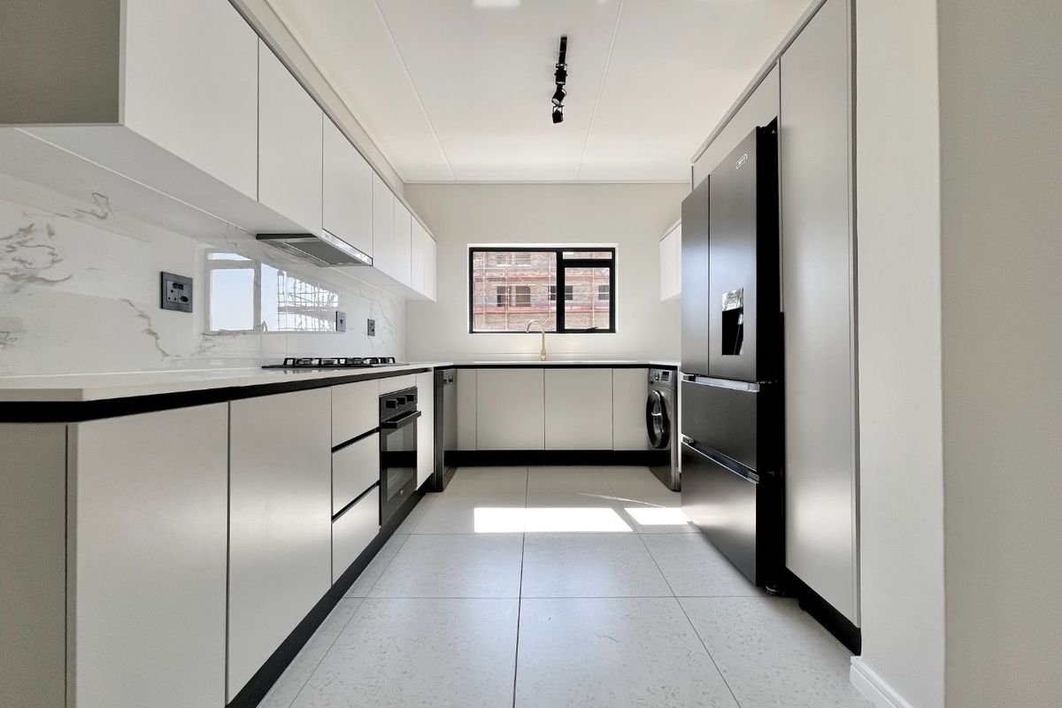 Modern galley-style kitchen featuring sleek white cabinetry, marble-look splashbacks, stone countertops, and high-quality integrated appliances in a bright, contemporary space.
