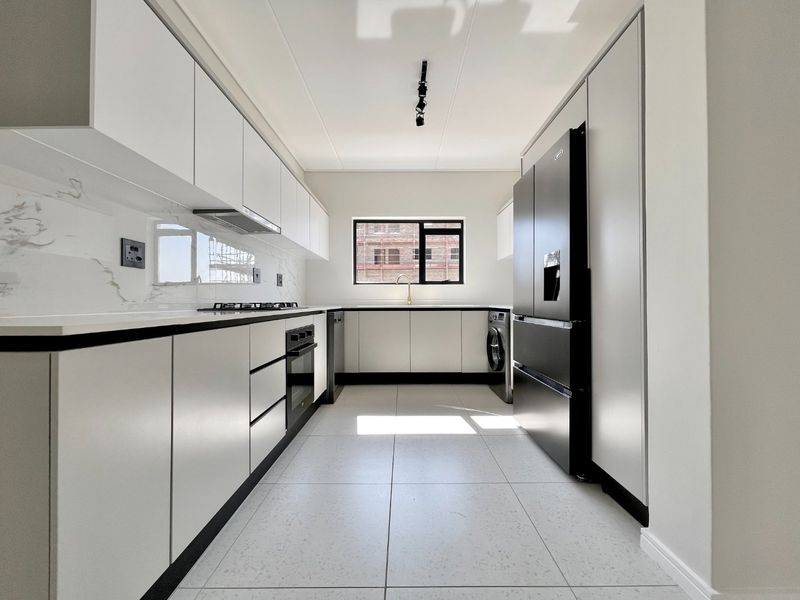 Modern galley-style kitchen featuring sleek white cabinetry, marble-look splashbacks, stone countertops, and high-quality integrated appliances in a bright, contemporary space.