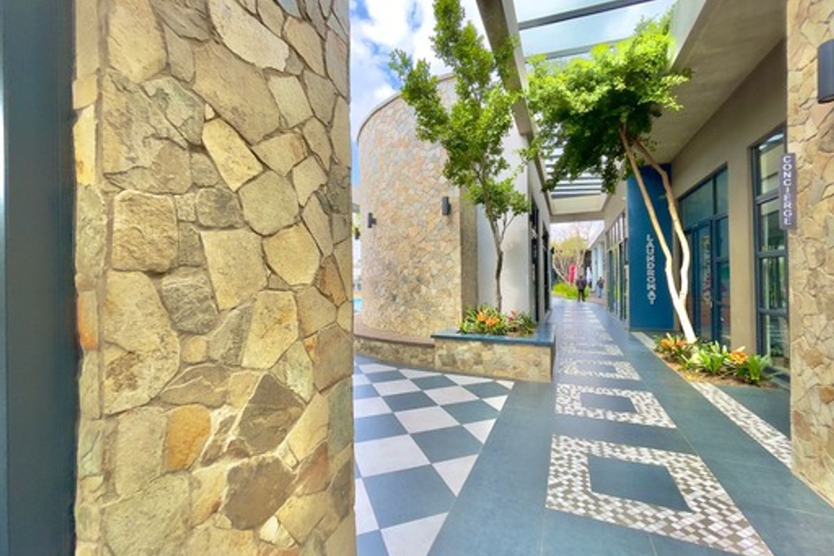 A well-maintained outdoor walkway featuring stone-clad pillars, a modern pergola, and decorative tiled flooring leading towards building facilities.