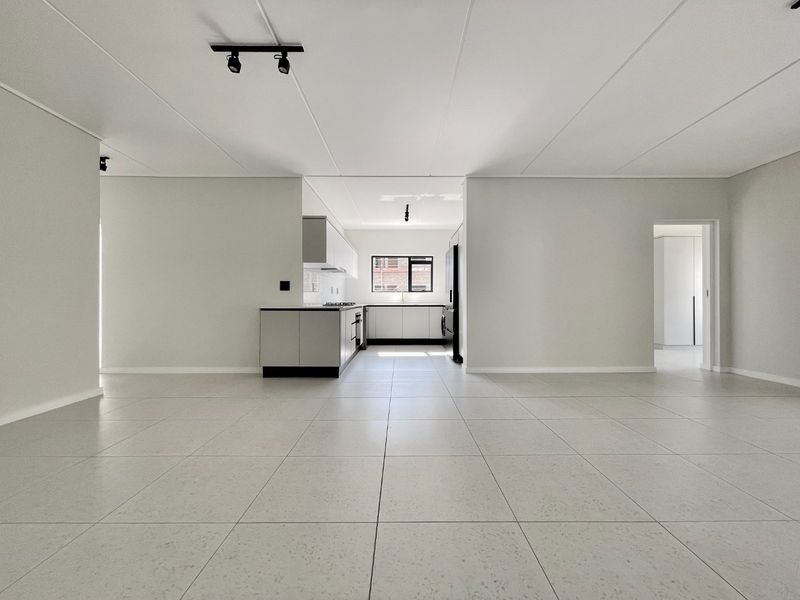 Spacious open-plan living area featuring modern tiled flooring, track lighting, and a sleek, minimalist kitchen with built-in cabinetry and appliances.