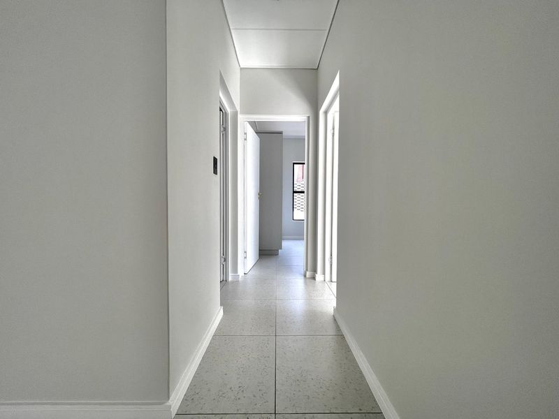 A clean, minimalist hallway featuring neutral walls and light-toned tiled flooring, providing a bright and seamless transition between rooms.