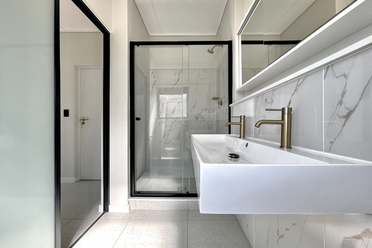 Modern bathroom featuring a floating double vanity with brass fixtures, marble-look wall tiles, and a spacious walk-in shower with a glass enclosure.