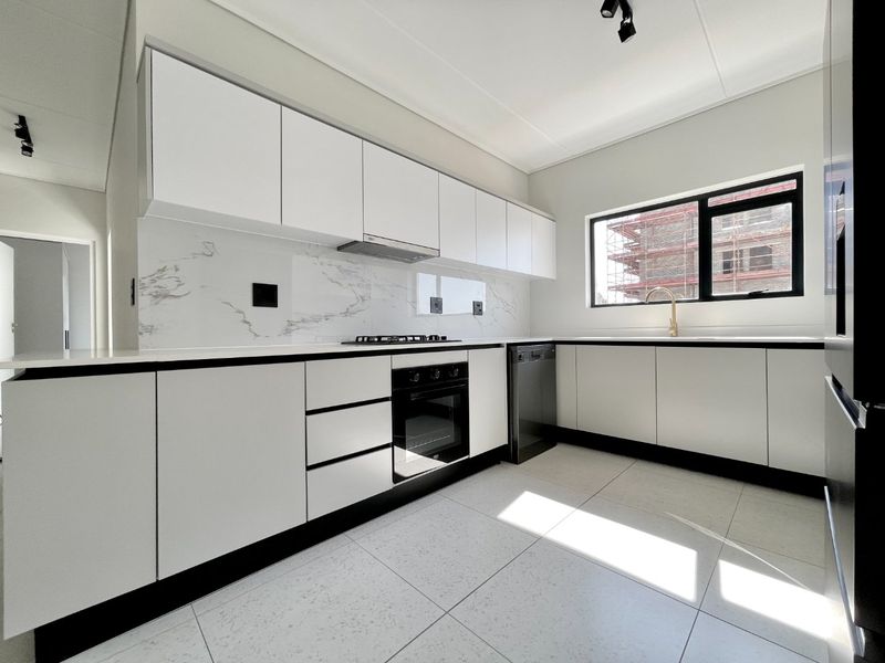 Modern kitchen featuring sleek white cabinetry, marble-look splashback, built-in oven, gas hob, and high-quality brass fixtures in a bright, clean space.