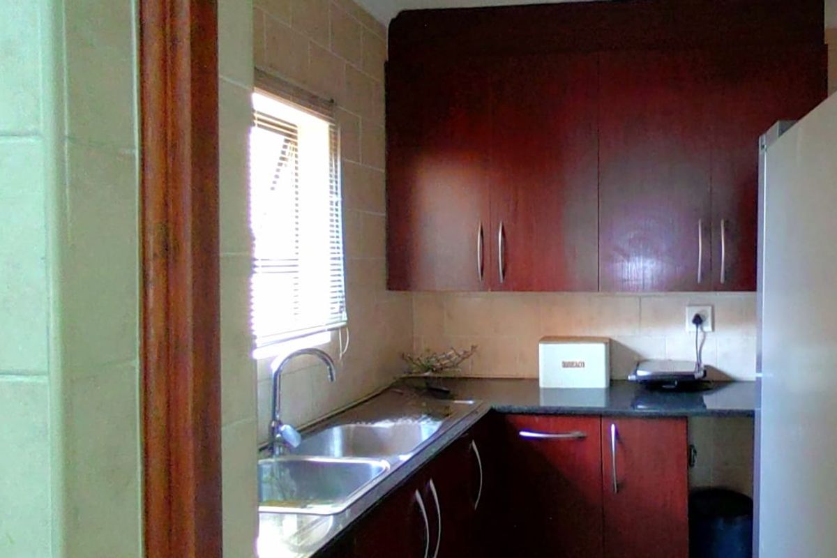A compact kitchen featuring dark wood cabinetry, laminate countertops, and a stainless steel double sink with a tiled backsplash.