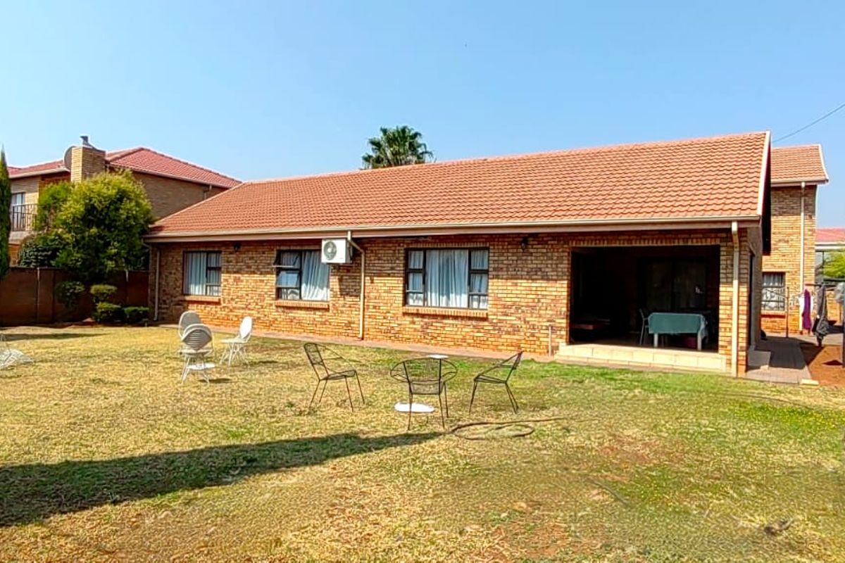 Rear view of a face brick house featuring a tiled roof, an integrated covered patio, and a spacious garden area.