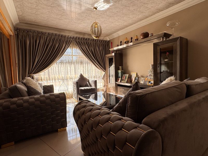 A comfortable living room featuring tiled flooring, a coved ceiling, and a built-in shelving unit, with natural light entering through a large sliding glass door.