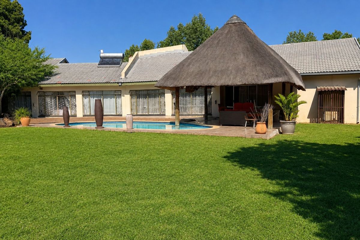 Rear view of the property featuring a spacious lawn, a swimming pool, and a covered thatch roof lapa area.