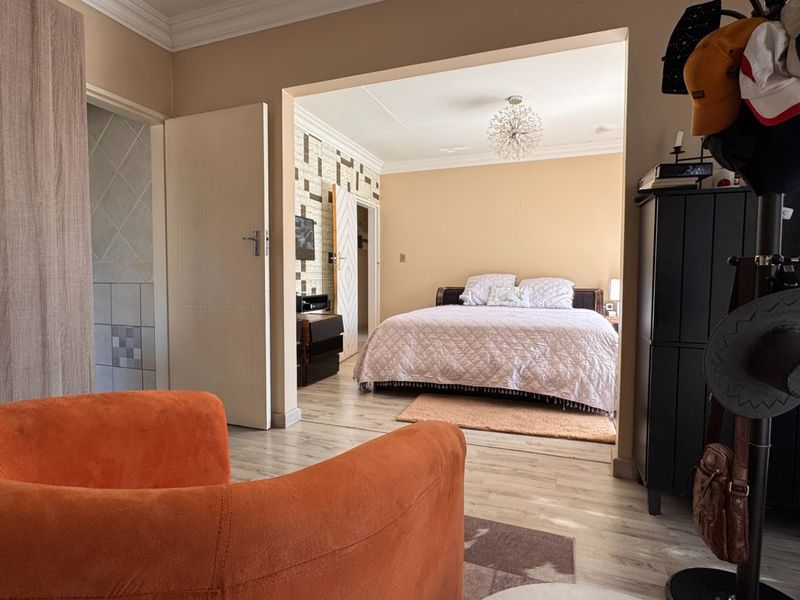 A bedroom featuring laminate flooring, built-in wardrobe storage, and decorative coving, viewed from an adjacent living space.