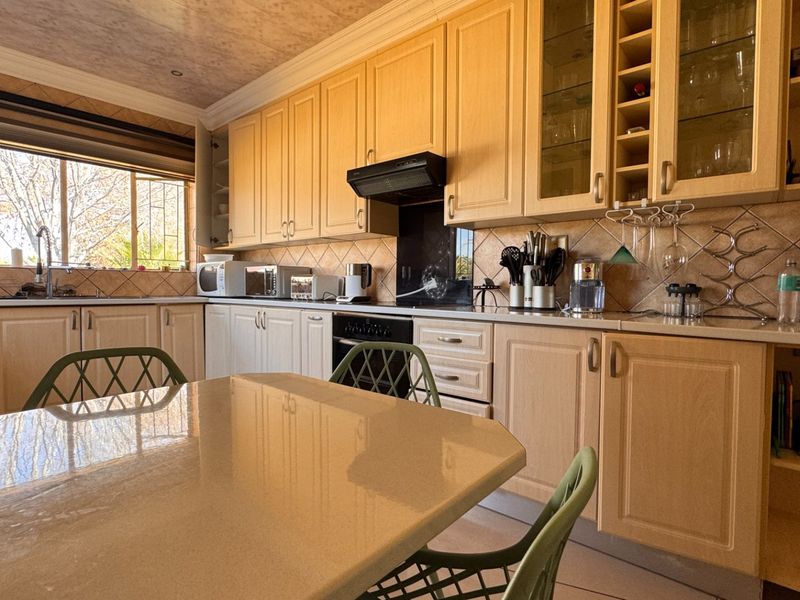 A functional kitchen featuring light wood cabinetry, stone countertops, a tiled backsplash, and integrated appliances, offering a classic and practical layout.