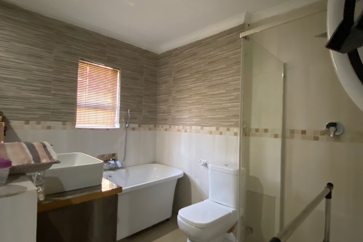 A functional bathroom featuring a freestanding bathtub, glass-enclosed shower, vessel sink, and neutral tiled finishes throughout.