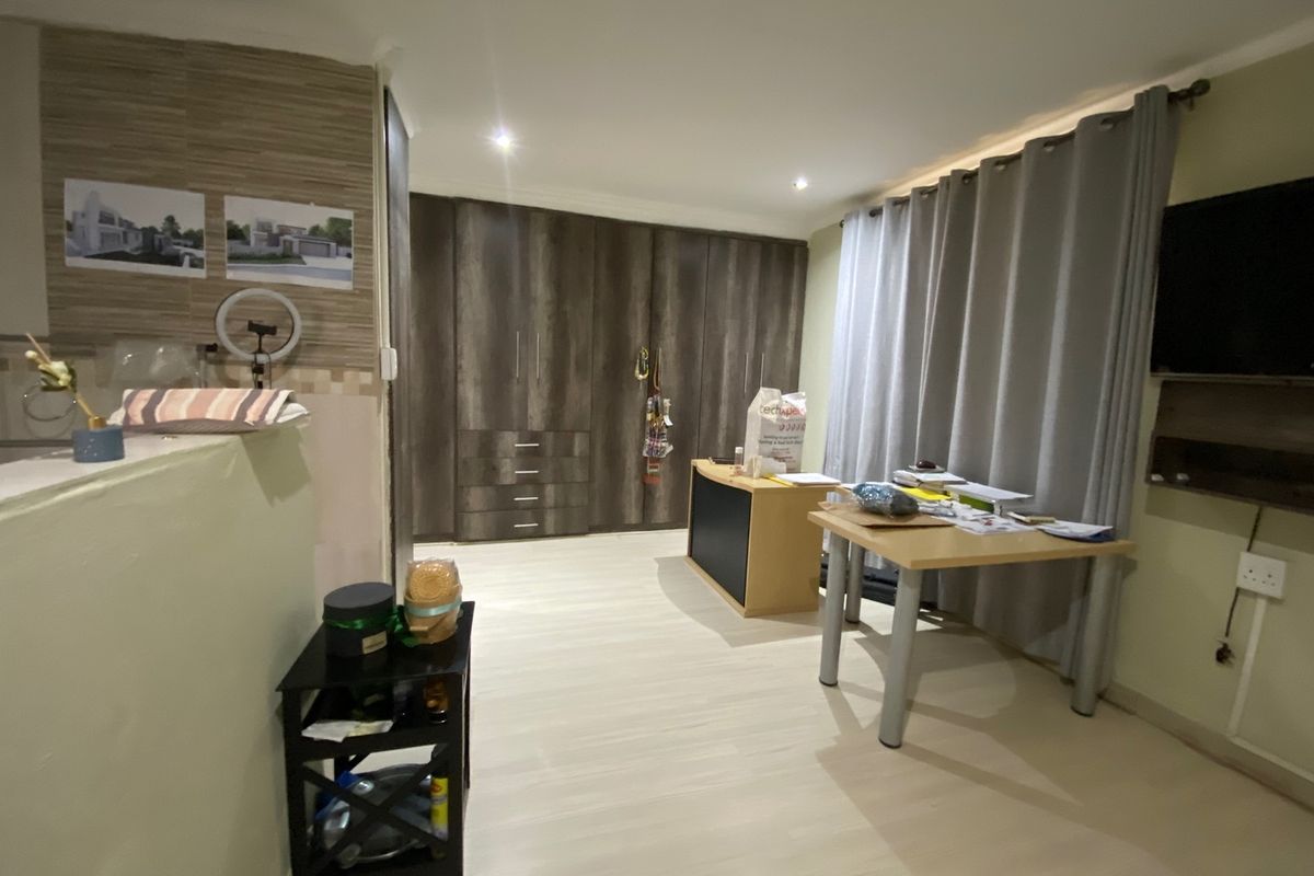 A bedroom featuring extensive built-in cupboards, recessed downlighting, and light-toned laminate flooring, offering a functional and neutral living space.