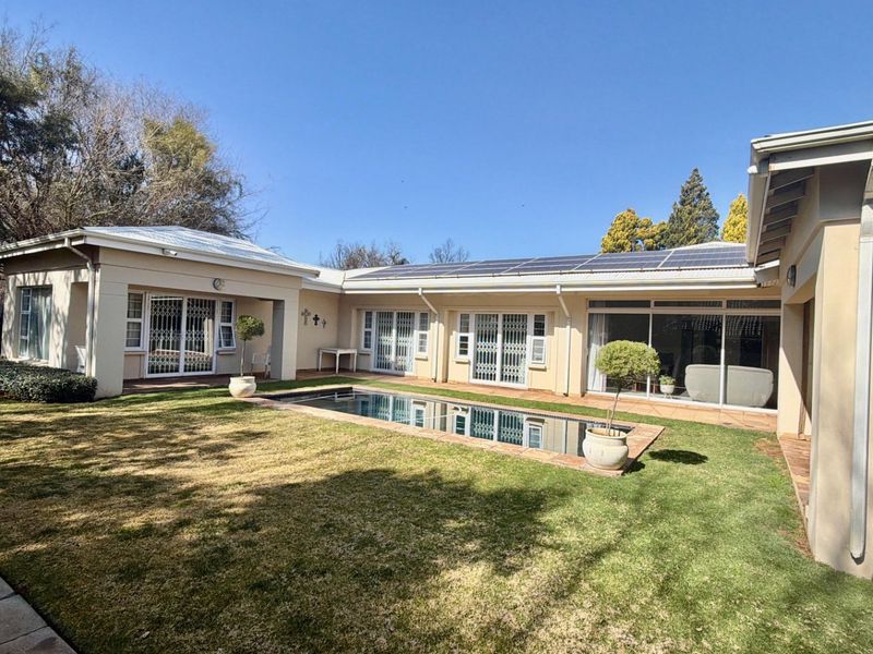 Rear view of the property featuring a well-maintained garden, a swimming pool, and solar panels installed on the roof.