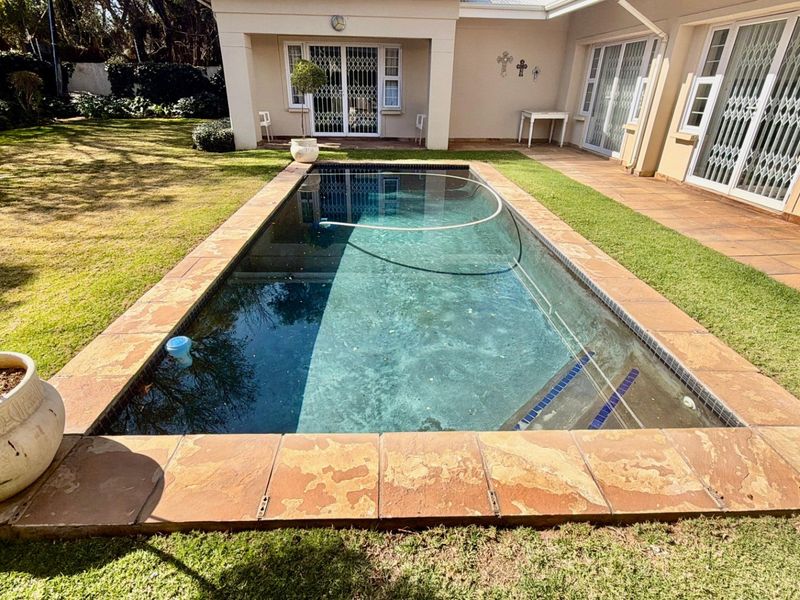 A rectangular swimming pool set in a landscaped garden with a paved patio area and direct access to the home via sliding doors.