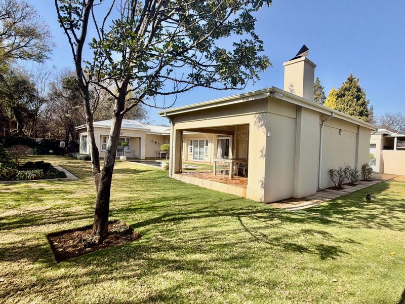 A well-maintained rear exterior view featuring a spacious covered patio with a masonry chimney, overlooking a manicured lawn and established garden.