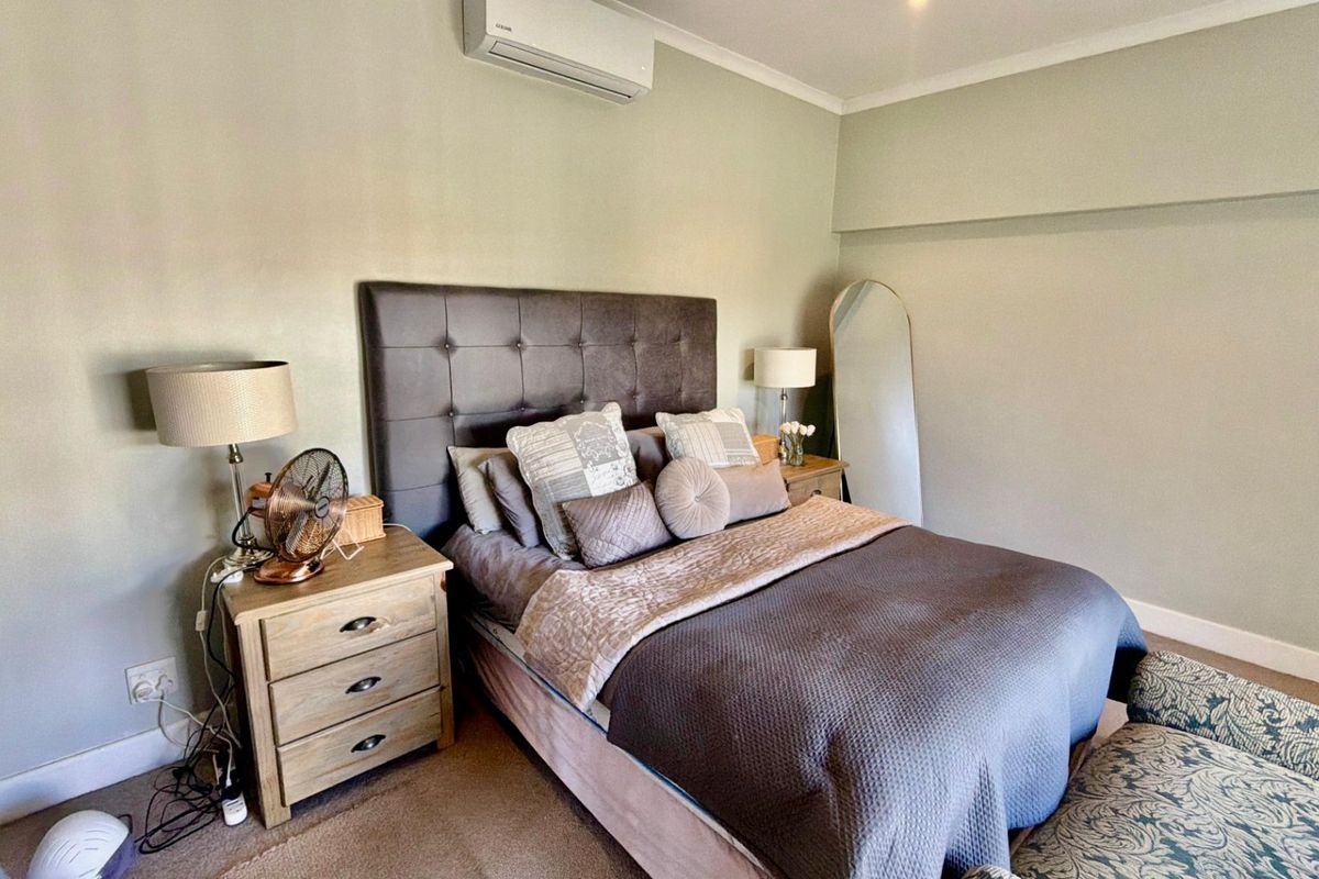 A well-maintained bedroom featuring a wall-mounted split-system air conditioner, neutral wall tones, and classic coving details.