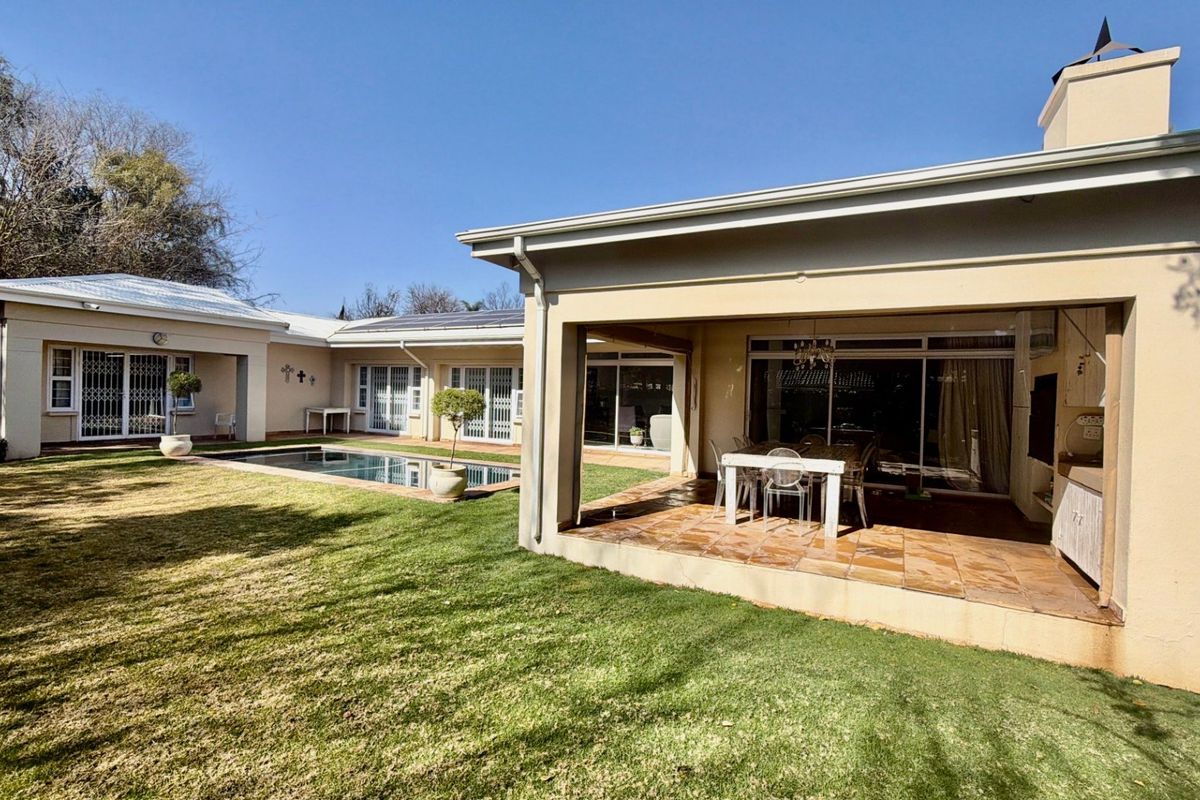 Spacious rear exterior featuring a covered patio, tiled flooring, built-in outdoor cabinetry, and a swimming pool set within a well-maintained garden.
