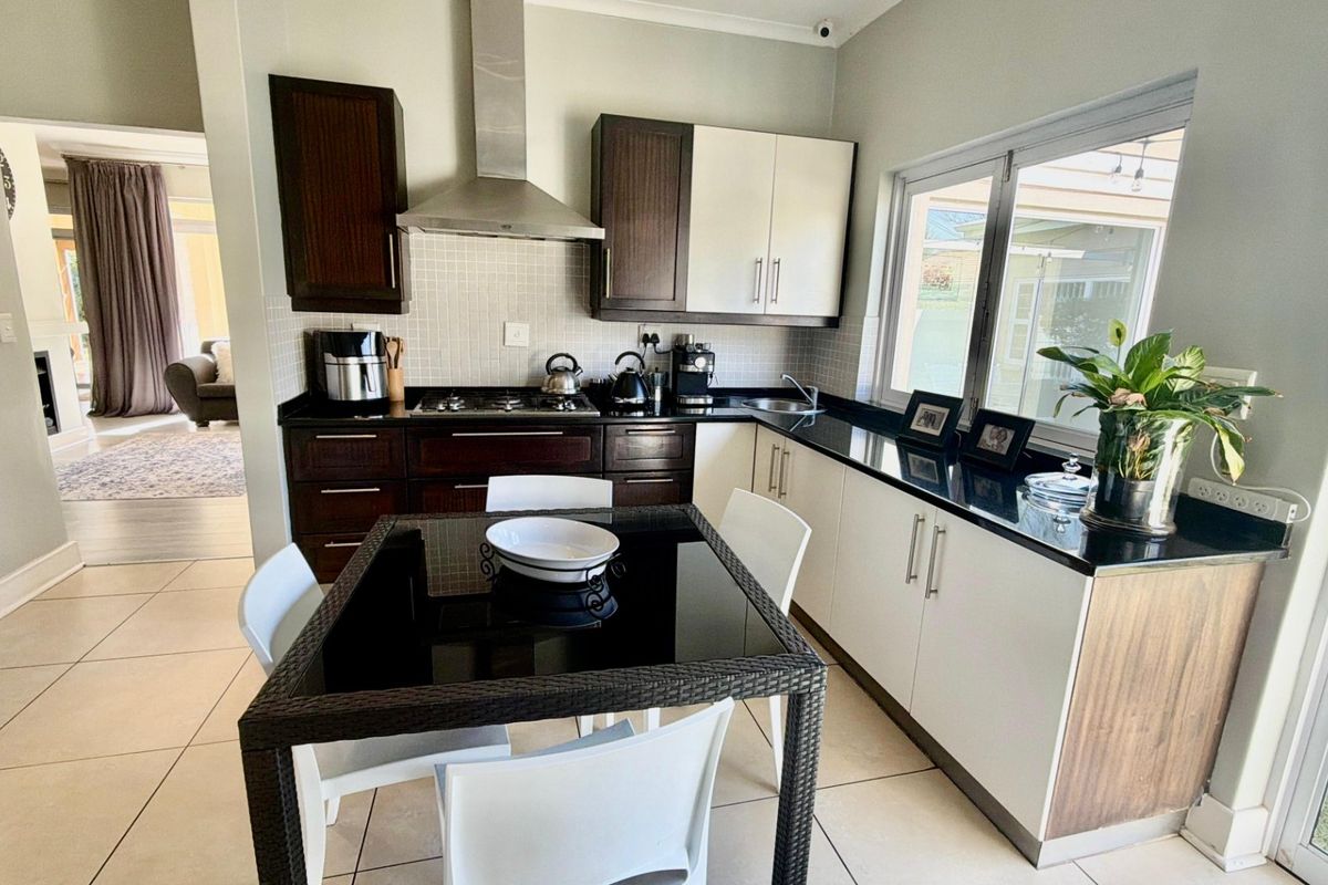 Modern kitchen featuring dark and light cabinetry, granite countertops, gas hob with extractor fan, and tiled flooring, with an adjacent dining area.
