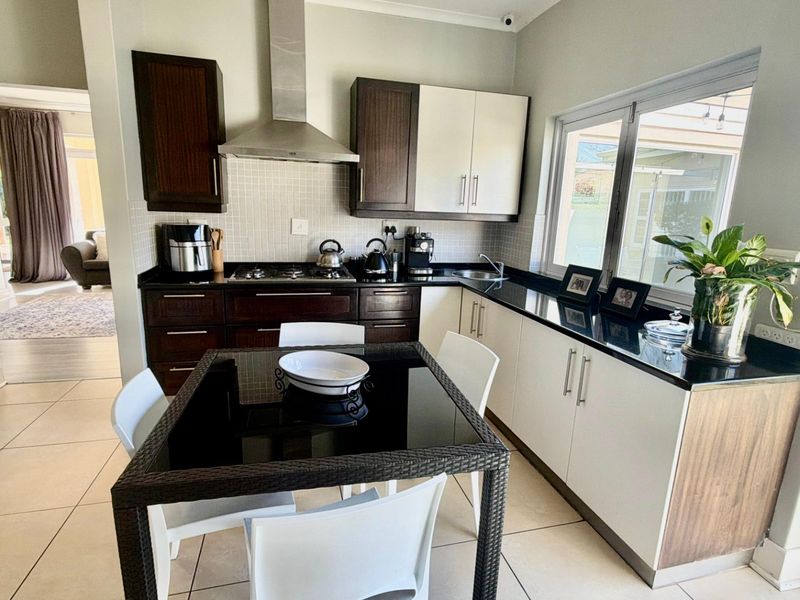 Modern kitchen featuring dark and light cabinetry, granite countertops, gas hob with extractor fan, and tiled flooring, with an adjacent dining area.