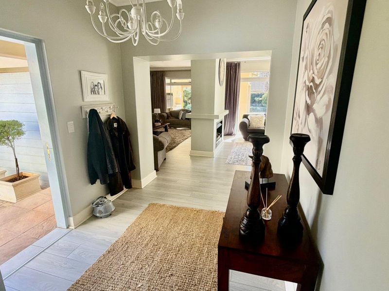 Welcoming entrance hall featuring light-toned laminate flooring and a chandelier, providing a clear view through to the adjacent living area with a built-in fireplace.