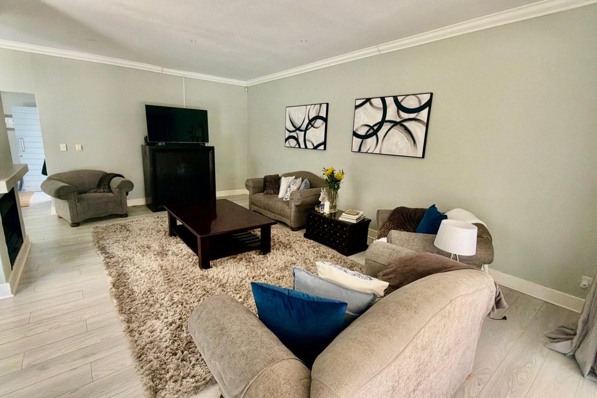 Spacious living room featuring light-toned laminate flooring, crown molding, recessed lighting, and a fireplace, creating a comfortable and well-maintained living space.