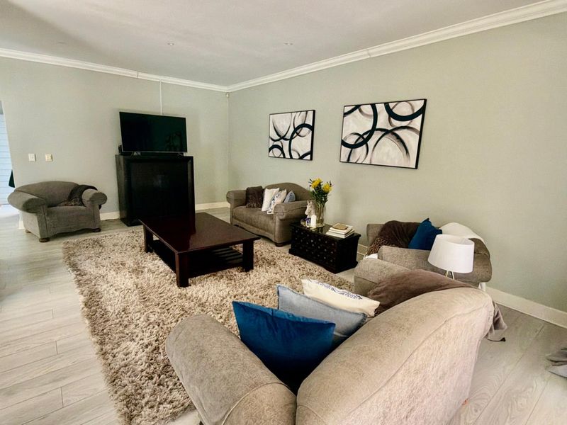 Spacious living room featuring light-toned laminate flooring, crown molding, recessed lighting, and a fireplace, creating a comfortable and well-maintained living space.