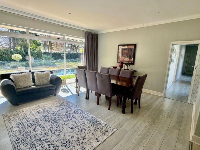 Spacious open-plan living and dining area featuring modern laminate flooring, recessed lighting, and large sliding doors providing seamless access to the garden and pool area.