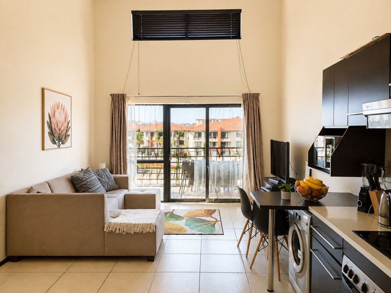 Modern open-plan living area featuring a compact kitchen with built-in appliances, high ceilings, and a sliding door leading to a private balcony.