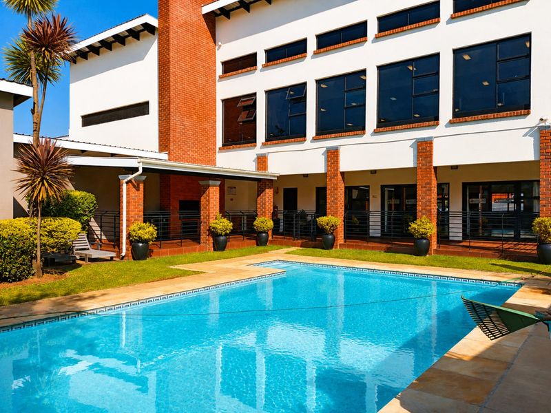 A well-maintained outdoor pool area featuring a swimming pool, covered patio space with brick pillars, and a prominent brick chimney feature.