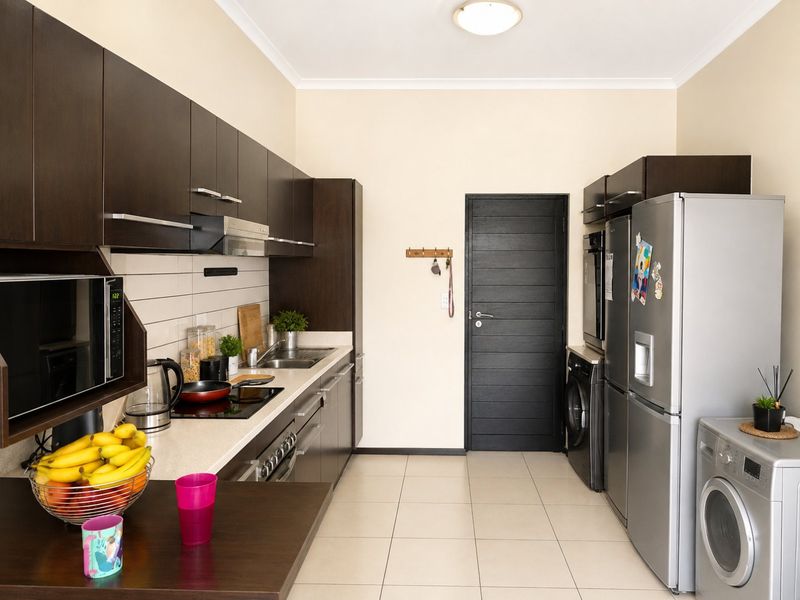 A functional kitchen featuring dark wood cabinetry, stone countertops, subway tile backsplash, and integrated appliances with tiled flooring.