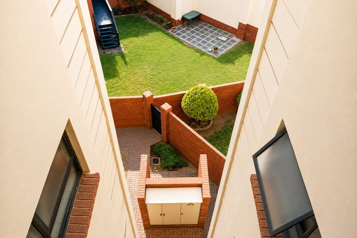 An elevated view of a private rear garden featuring a paved courtyard, lawn area, and brick boundary walls within an apartment complex.