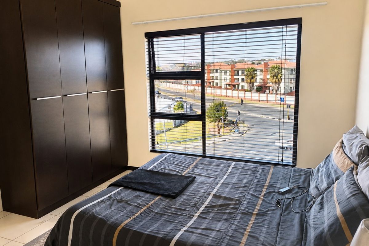 A well-maintained bedroom featuring dark built-in wardrobes, tiled flooring, and large windows with venetian blinds offering an urban street view.